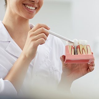 dentist showing a patient a model of a dental implant in the jaw 