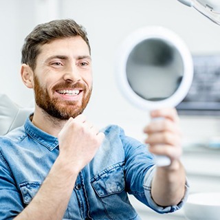 man admiring his new smile after receiving his dental implant restorations