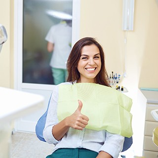 Woman smiling and giving a thumbs up in dental chair