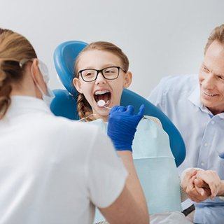 A child completing a dental exam with her parent.