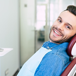 Man in a denim shirt smiling and leaning back in the dental chair
