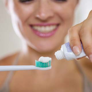 person putting toothpaste onto an electric toothbrush