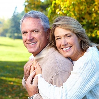 An older couple smiling and hugging outside.