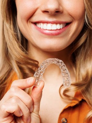 Woman smiling while holding a clear aligner tray