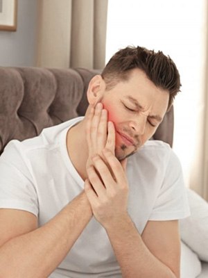 Man sitting in bed rubbing his aching jaw