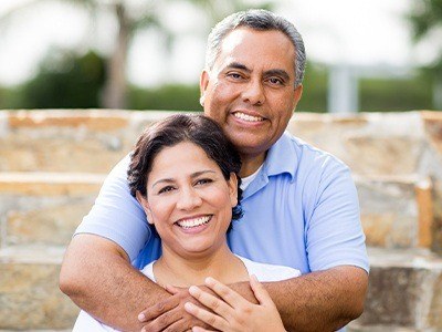 Smiling older man and woman outdoors after replacing missing teeth