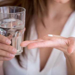 Woman holding glass of water and white pill for oral conscious sedation in Pembroke Pines